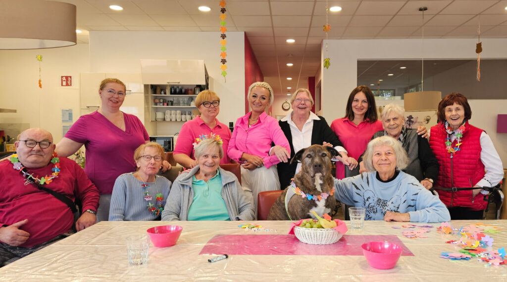 Gäste und Mitarbeitende sitzen gemeinsam am Tisch, lachen und basteln in einem hellen Raum der Tagespflege.