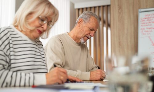 Seniorenpaar füllt Formulare am Tisch aus – Beratung zu Pflegekasse und Pflegegrad.